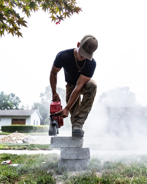 Crew member cutting hardscape block during a patio and wall installation